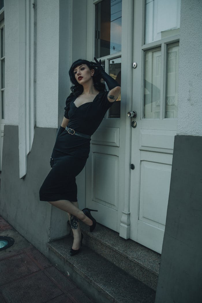 about-us-01 Elegant woman in black dress poses against classic doorway, evoking timeless style.